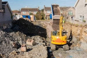 Excavator is digging a house foundation in a residential area while a dumper truck is unloading construction gravel, sand and crushed stones on the construction site. excavation for house foundation contracting