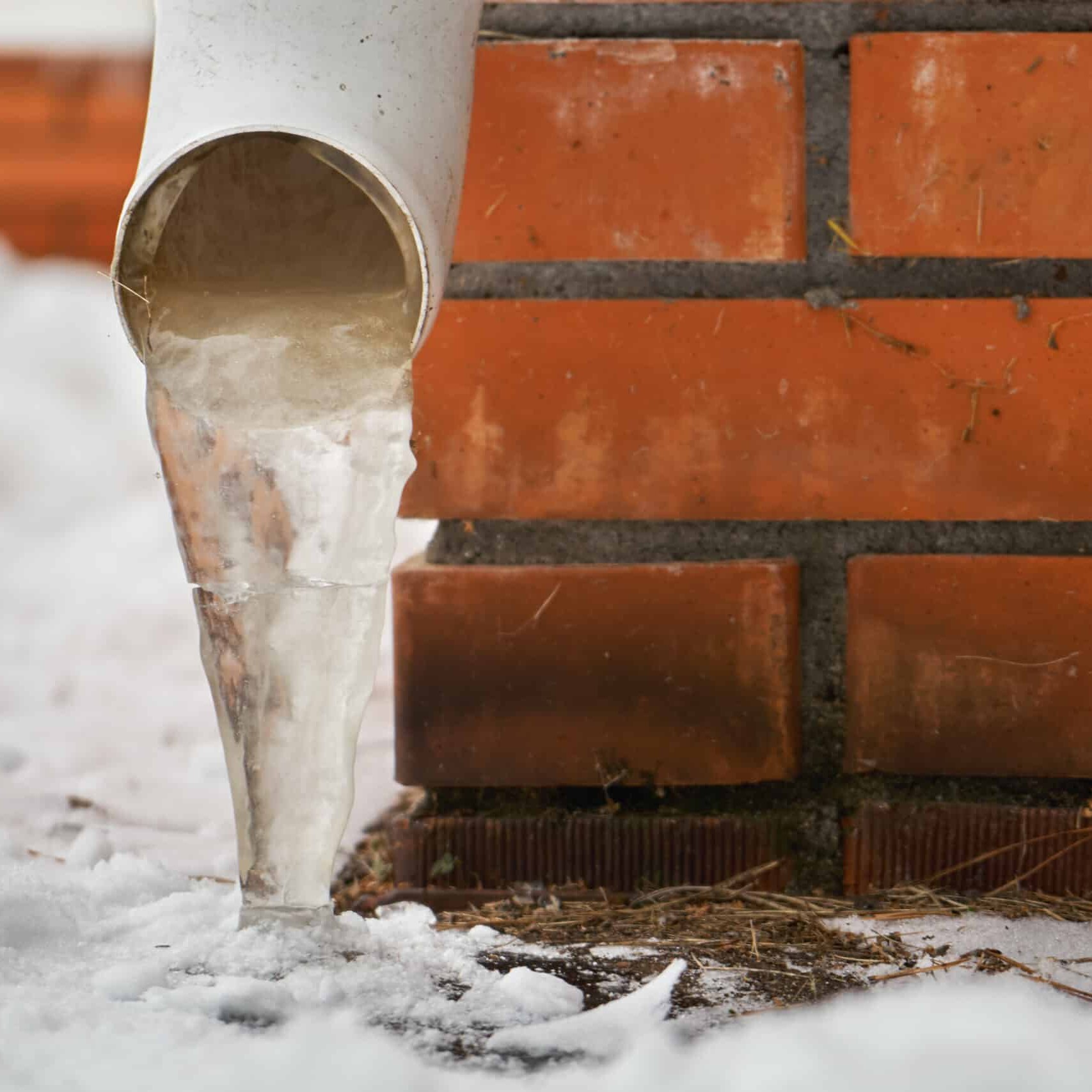 Drain pipe with frozen stream of water near house brick wall