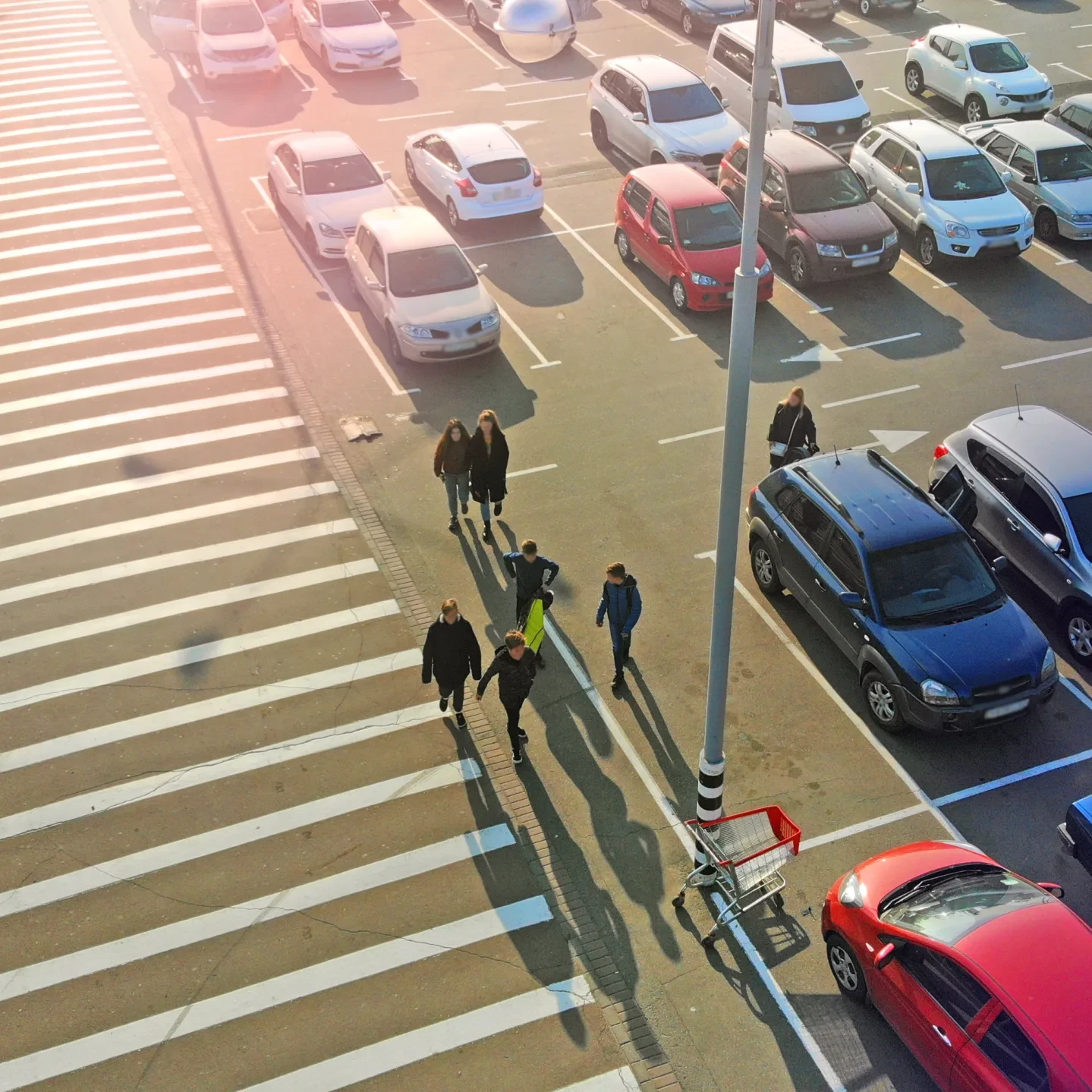 Pedestrian crossing and parking lot next to the entrance of a mall. Aerial. People go to the mall.