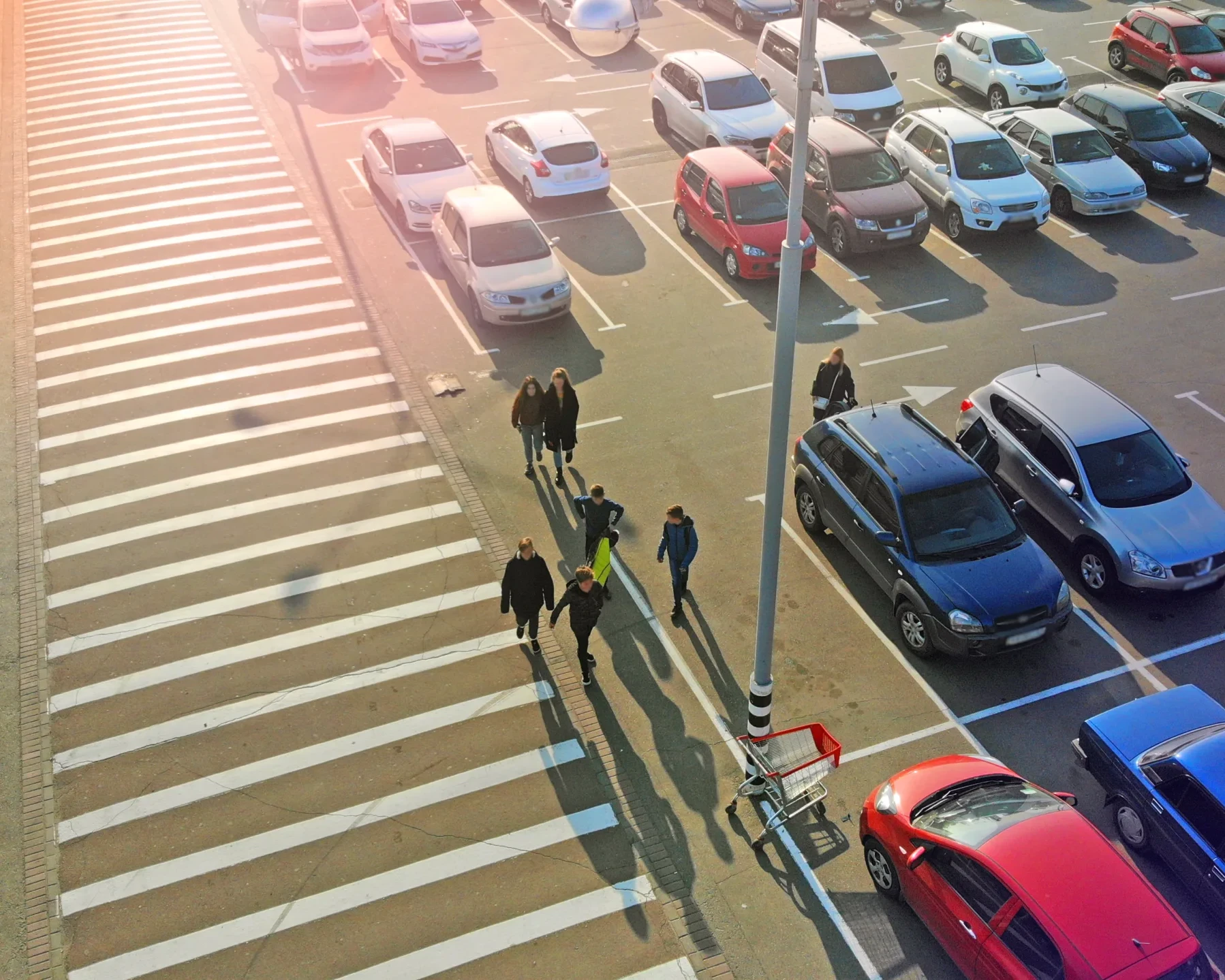 Pedestrian crossing and parking lot next to the entrance of a mall. Aerial. People go to the mall.