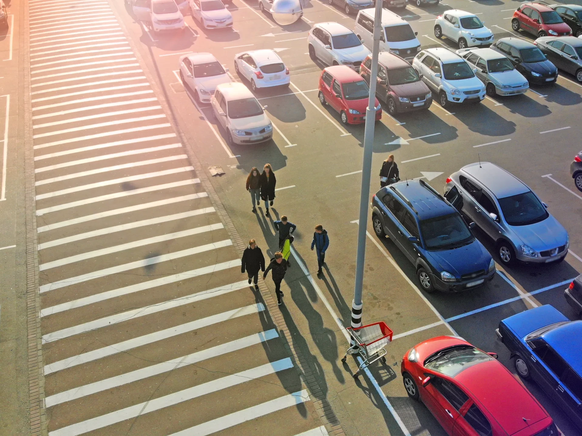 Pedestrian crossing and parking lot next to the entrance of a mall. Aerial. People go to the mall.