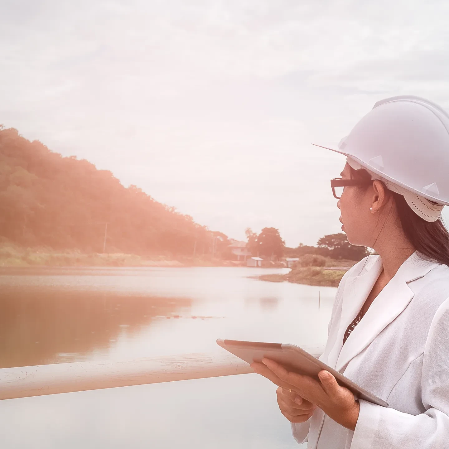 Female engineer in a white helmet working with a digital tablet and looking away at the dam construction site to generate electricity.