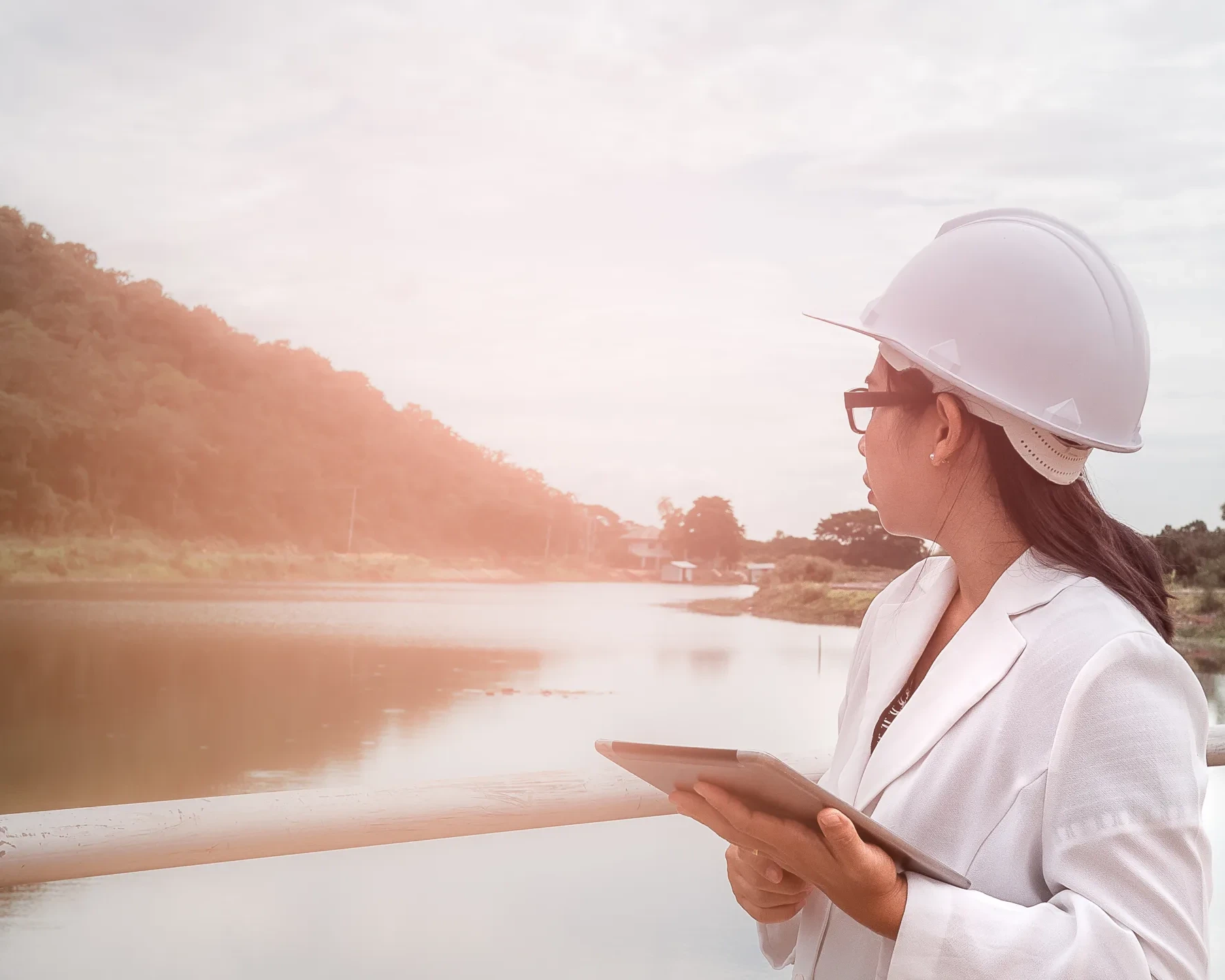 Female engineer in a white helmet working with a digital tablet and looking away at the dam construction site to generate electricity.