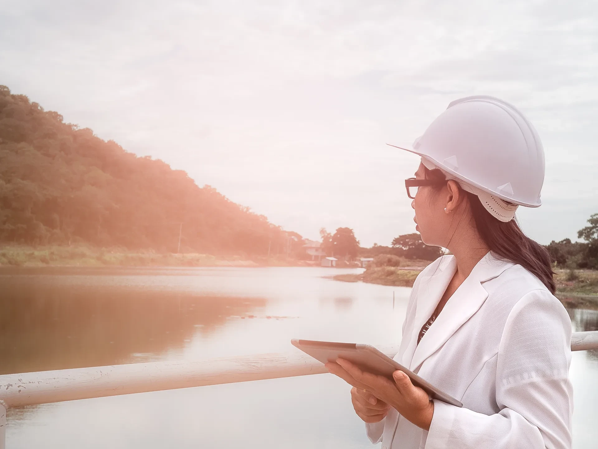 Female engineer in a white helmet working with a digital tablet and looking away at the dam construction site to generate electricity.