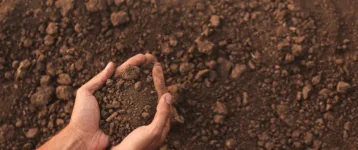 Male farmer with heap of soil in field, top view