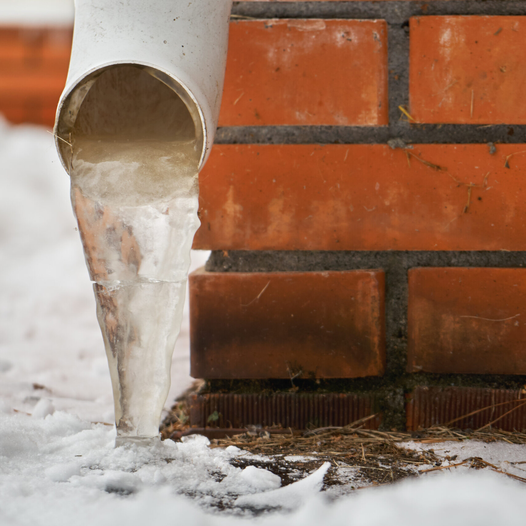 Drain pipe with frozen stream of water near house brick wall