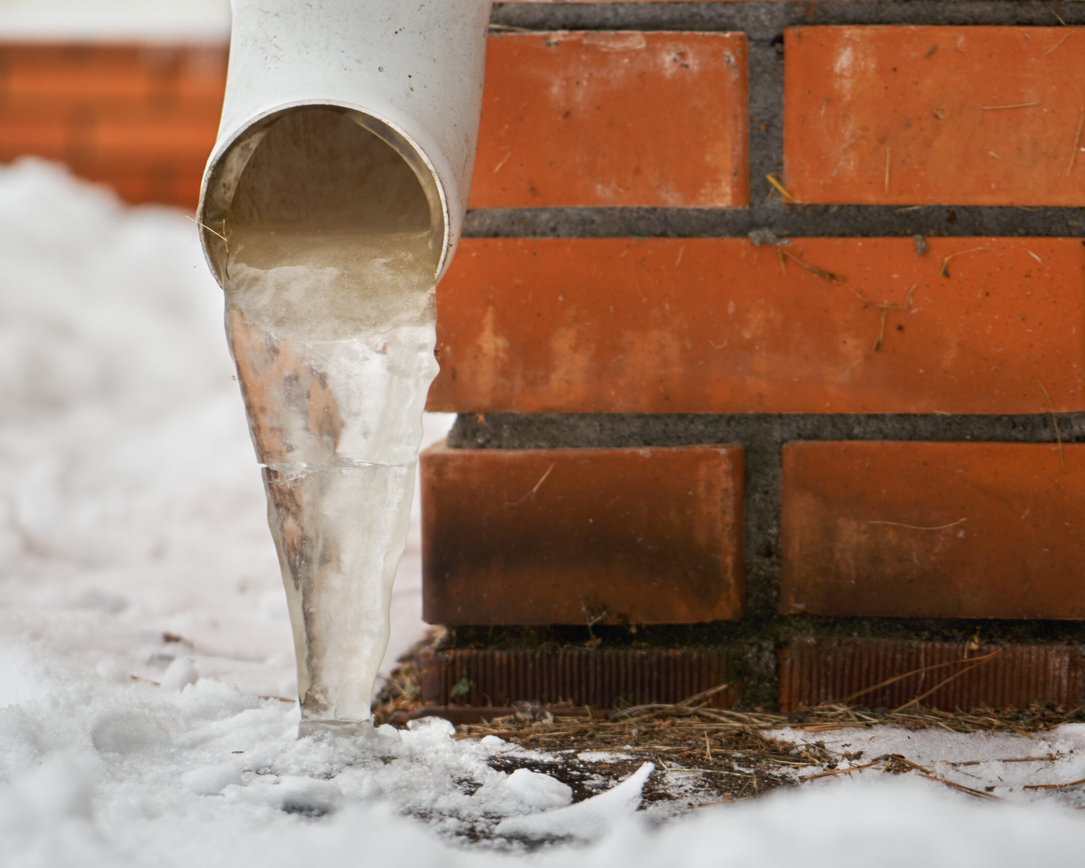 Drain pipe with frozen stream of water near house brick wall