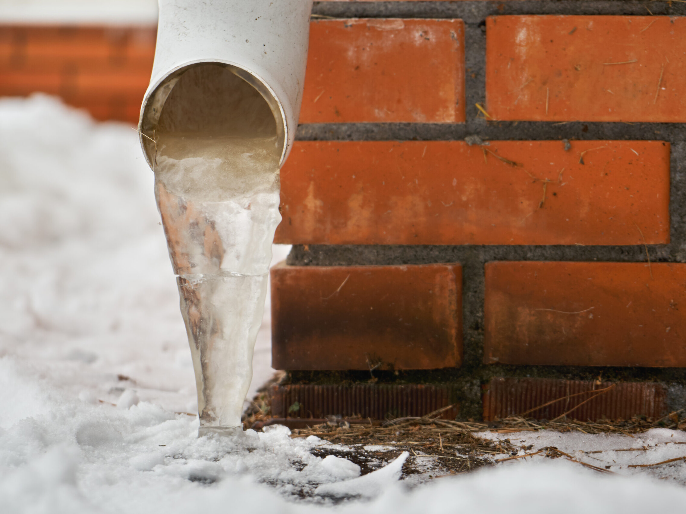 Drain pipe with frozen stream of water near house brick wall
