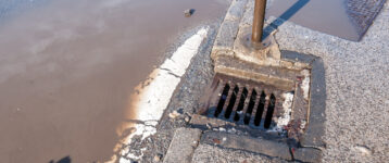 Drainage or sewage manhole grid system on the street asphalt road useless because of damaged tarmac with pot hole full of water after heavy rain and melted snow in the winter season