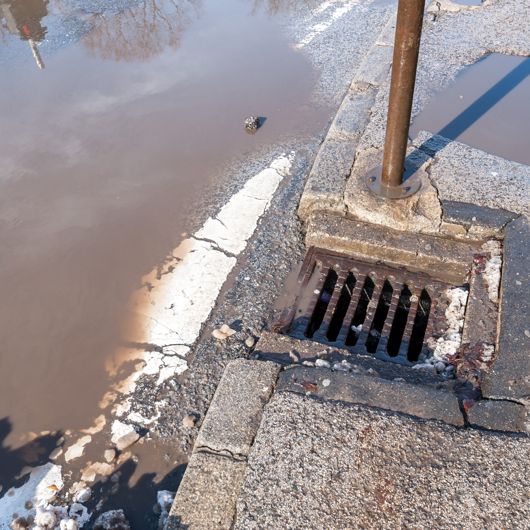 Drainage or sewage manhole grid system on the street asphalt road useless because of damaged tarmac with pot hole full of water after heavy rain and melted snow in the winter season